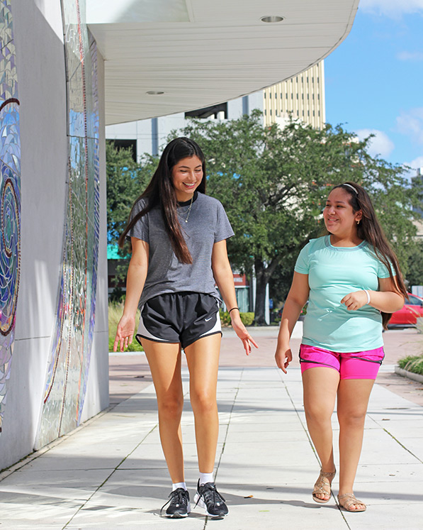 A big sister walking and smiling with a little sister.