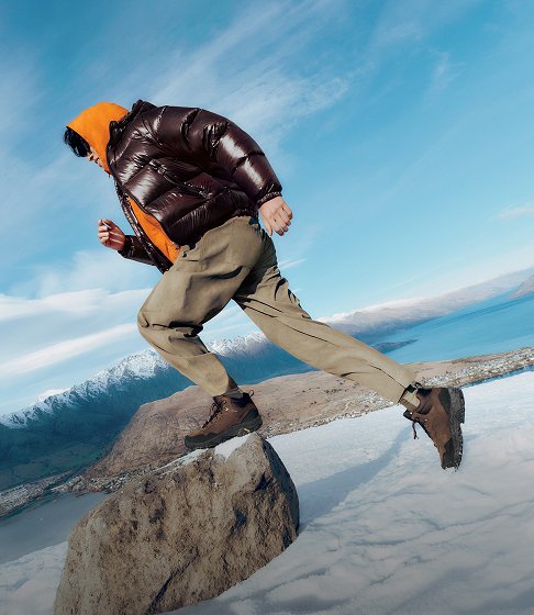 Hiker in Merrell winter boots stepping across rocks in a snowy mountain landscape.