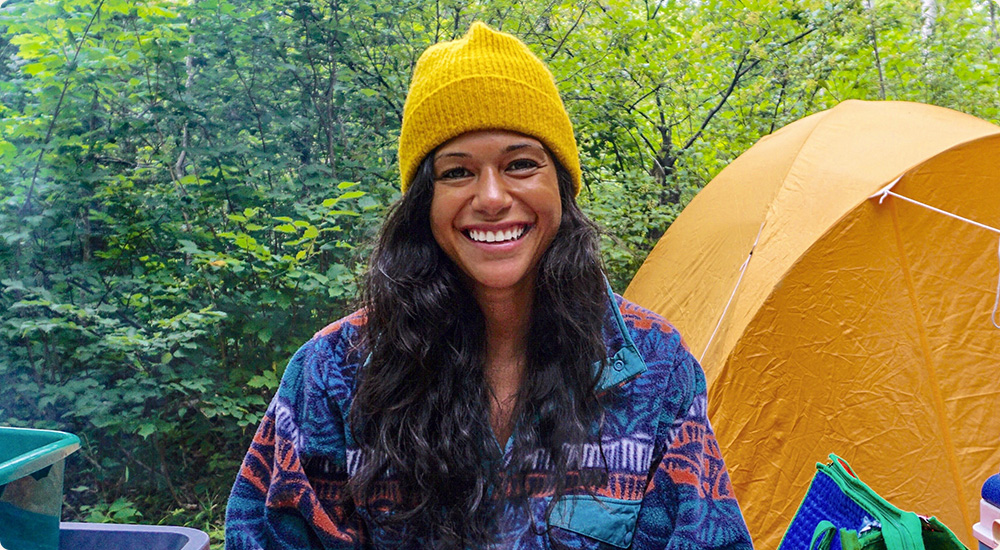 Mary Soueidan standing in the wood beside a yellow tent.