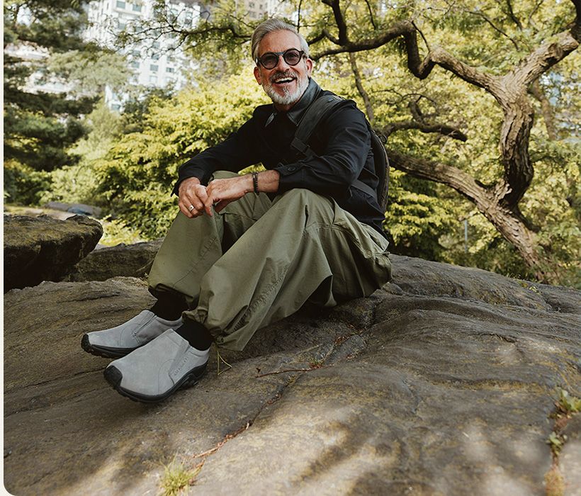 A person sitting on a rock wearing Merrell Jungle Moc shoes.