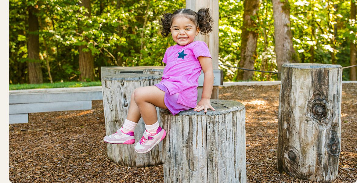 A girl sitting on a stump wearing Merrell shoes.