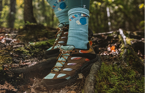 A person's feet in a forest wearing Merrell Moab hiking shoes.