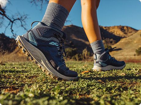 A person's feet in a grassy area wearing Merrell hiking shoes.