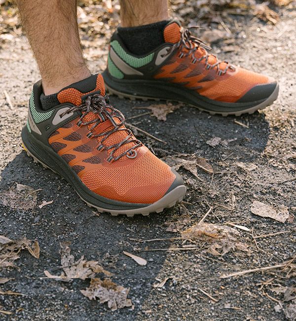 A person's feet in orange and green Nova hiking shoes.