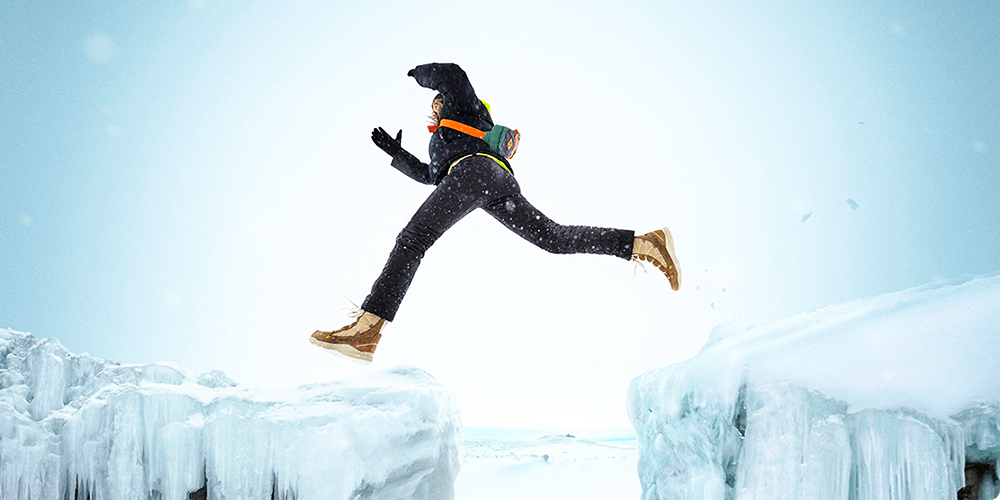 Someone jumping from one iced rock to the other wearing Merrell winter gear.