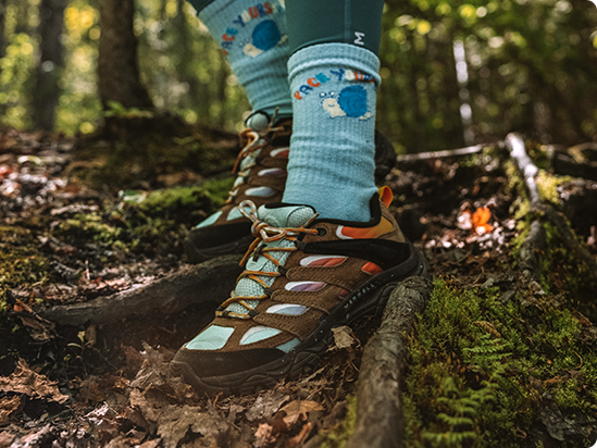 A person's feet in a forest wearing Merrell Moab hiking shoes.