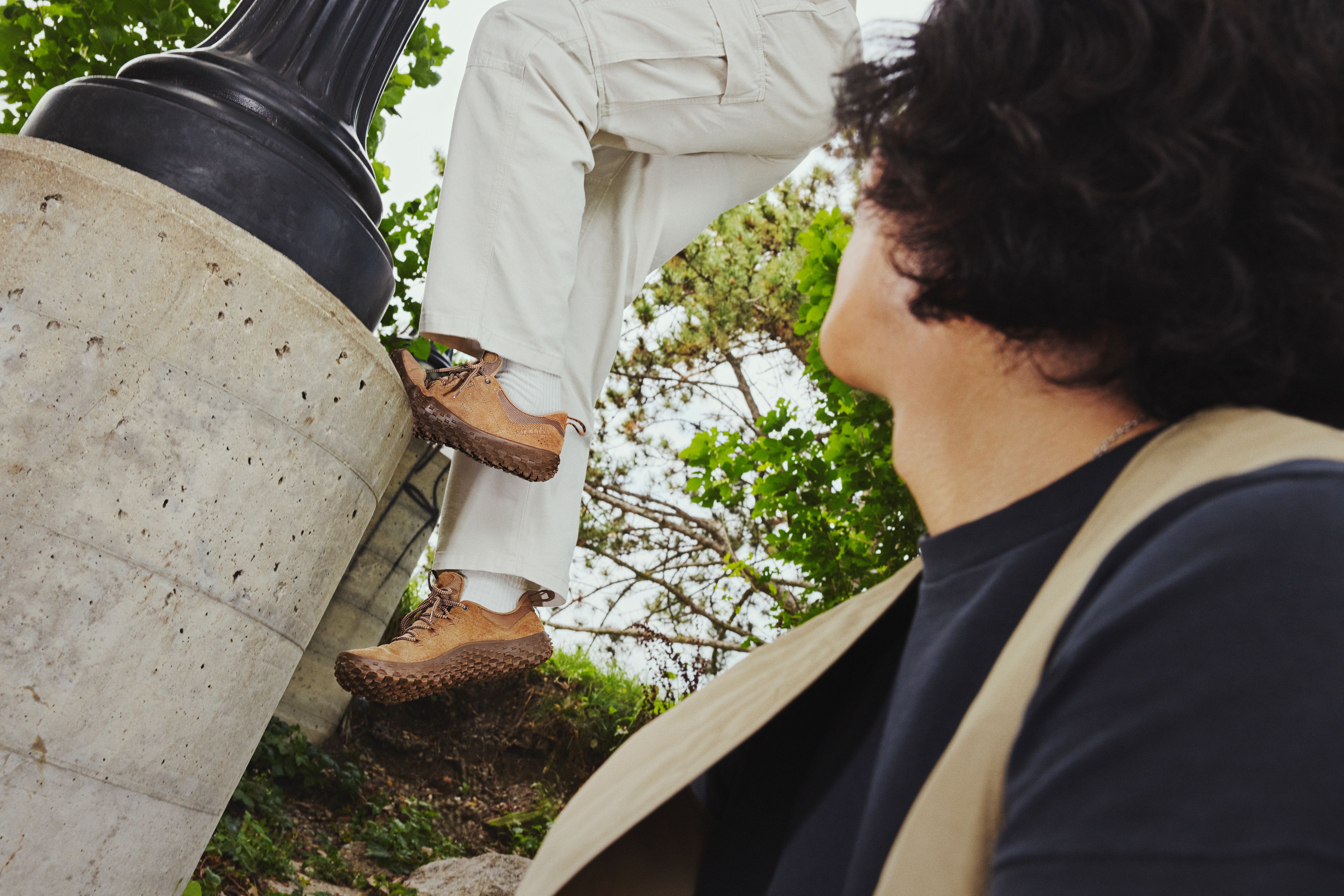 Person stepping on concrete ledge outdoors wearing Merrell barefoot shoes