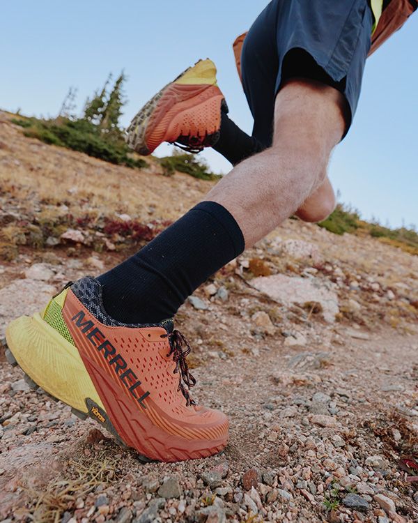 Les jambes et les pieds d'une personne portant la chaussure Merrell Agility Peak 5 dans une zone rocheuse.