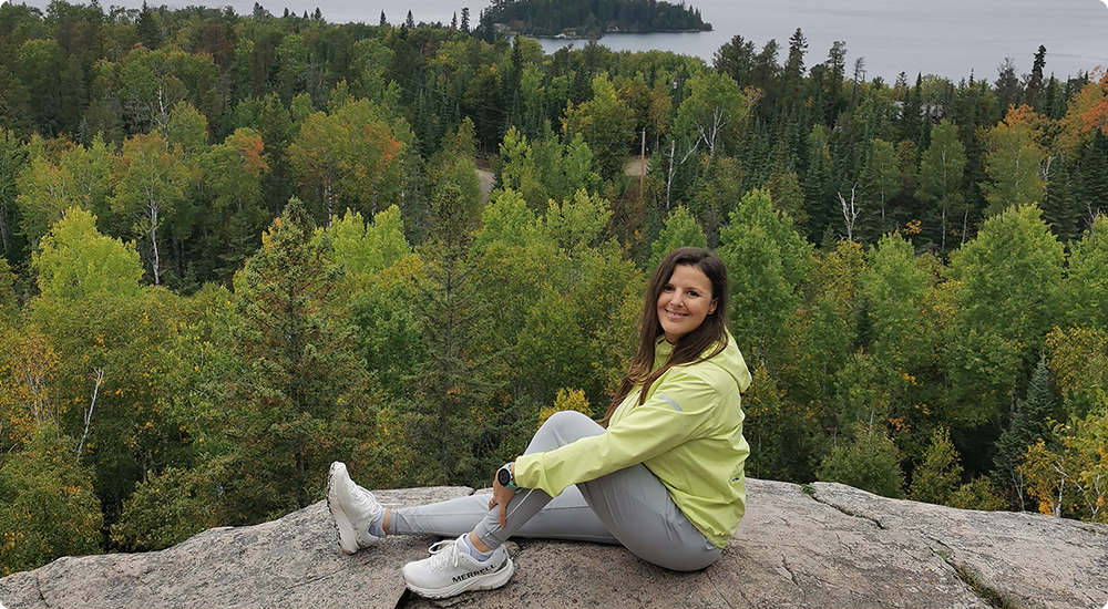 Ashley Moore assise sur un rocher avec des arbres et de l'eau en arrière-plan.