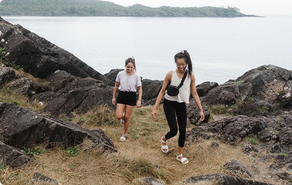 Two people walking on a rocky shore wearing Merrell sandals.