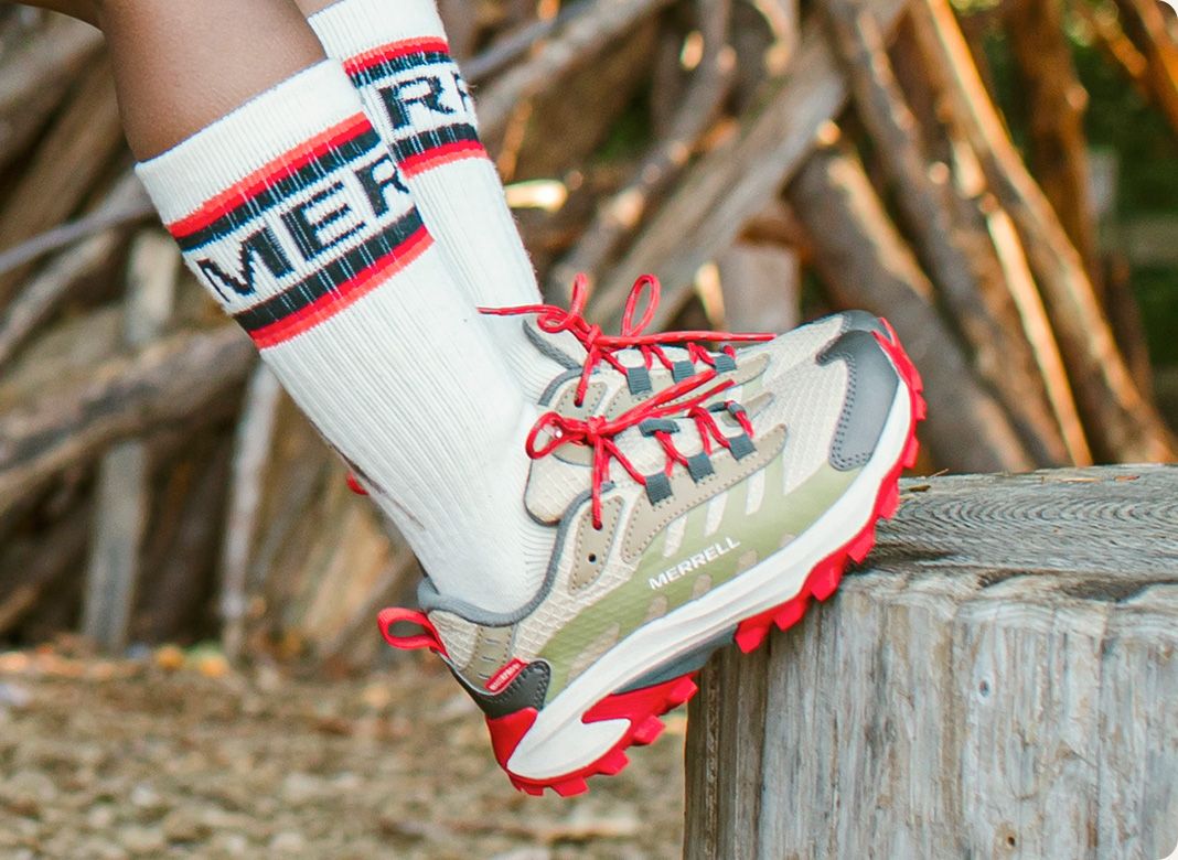 A person's feet wearing white socks and red and white Merrell shoes.