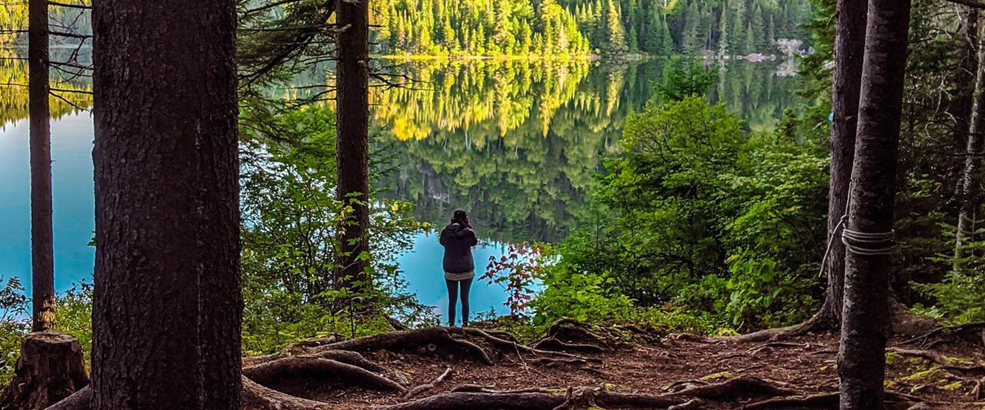 Mary Soueidan standing in the wood beside the lake wearing Merrell gear.