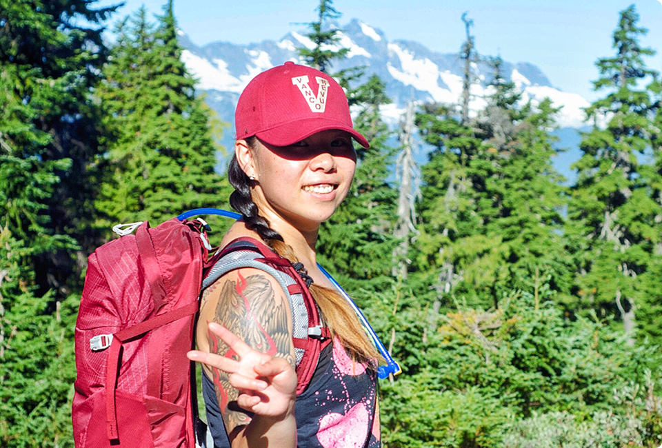 Tilly Tseng avec un sac à dos et un chapeau rouge devant des arbres.