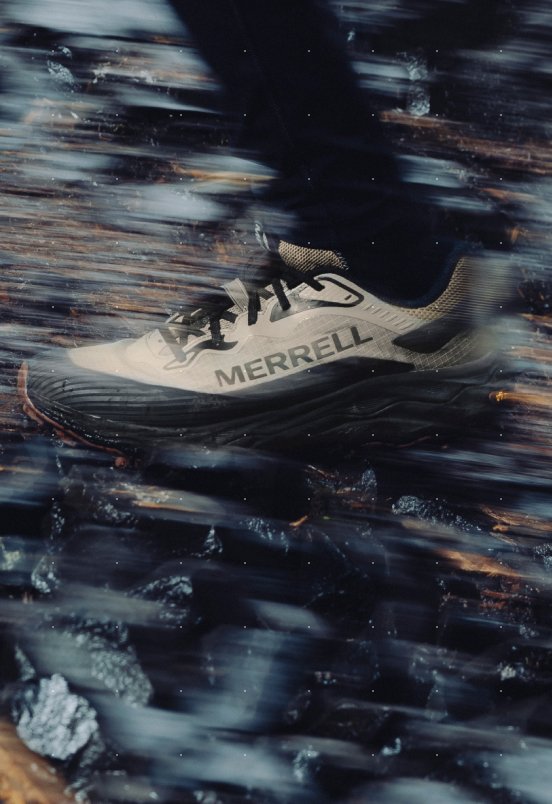 A Merrell shoe in motion, stepping over a blurred rocky trail.
