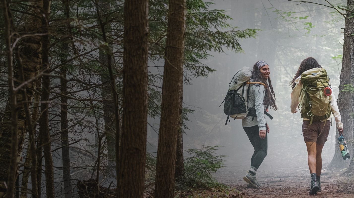 Two women backpacking in a foggy woods, wearing Merrell Bravada hiking shoes