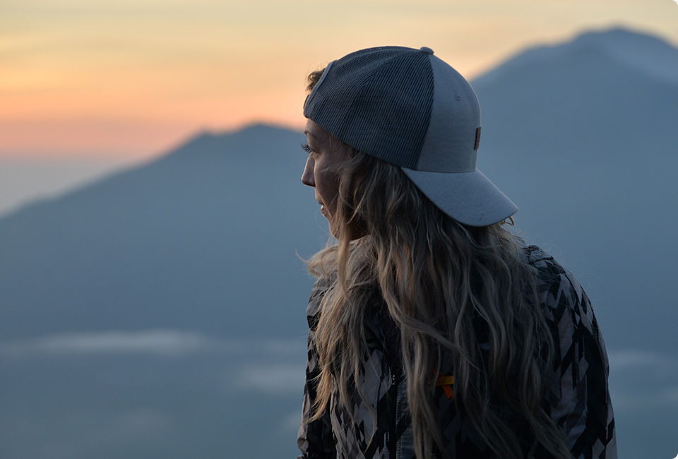 Audrey Normandeau sitting wearing a cap and looking at mountains.