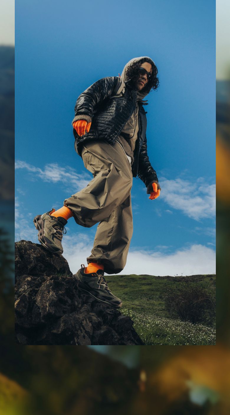 Person in a black puffer jacket standing on a rocky outcrop above a lake.