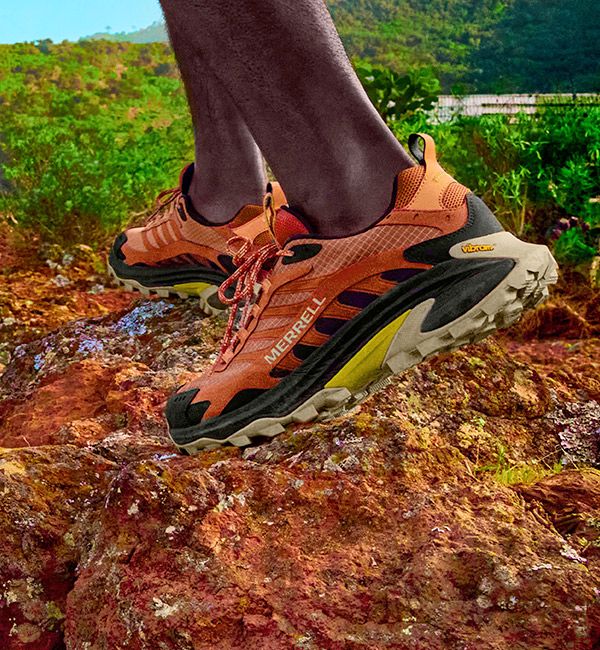 A person's feet in orange Moab Speed 2 hiking shoes on a rocky surface.