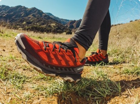 Les pieds d'une personne dans un champ portant des chaussures de randonnée Merrell.