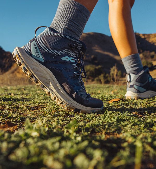 A person's feet in Antora hiking shoes in a field.
