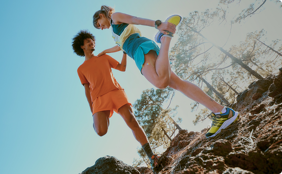 Two people stretching on a rocky hill wearing Merrell gear.