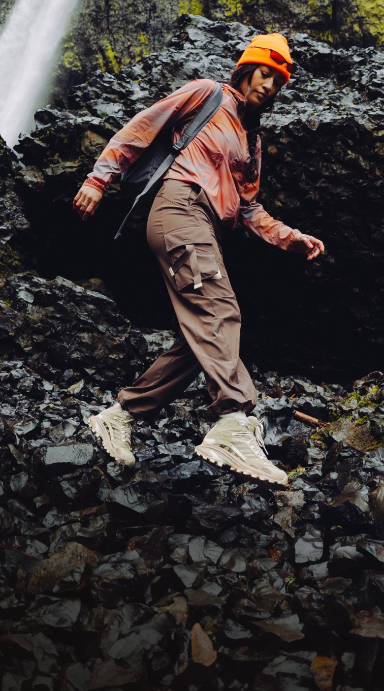 A hiker in Merrell Moab Speed 2 shoes stepping across dark volcanic rocks near a waterfall.