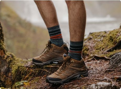 Les jambes d'une personne dans des chaussures de randonnée Merrell brunes et des chaussettes.