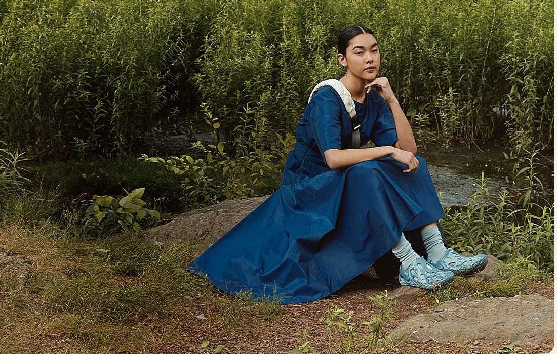 A person in a blue dress sitting on a rock wearing Merrell Hydro Moc shoes.