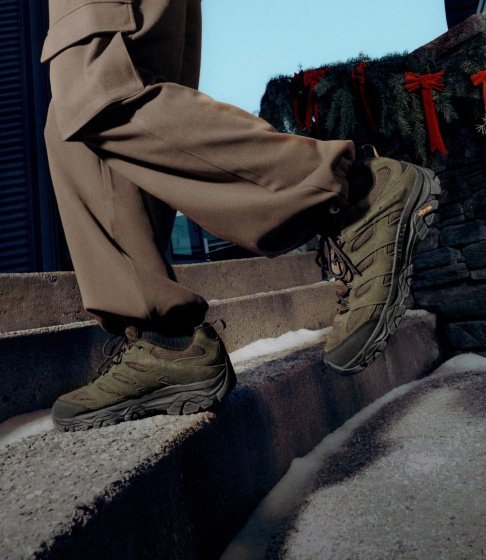 Person in olive Merrell hiking shoes walking up snowy stone steps decorated with greenery and red bows.