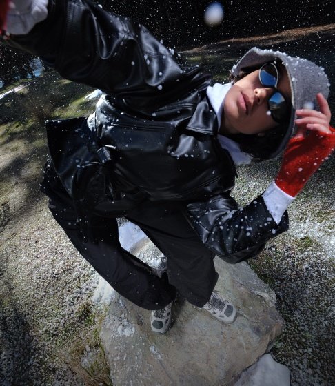 Person in a black puffer jacket, sunglasses and red gloves posing in the falling snow in Merrell shoes.