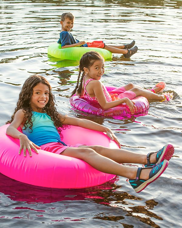 A group of kids floating on inner tubes in water wearing Merrell shoes.