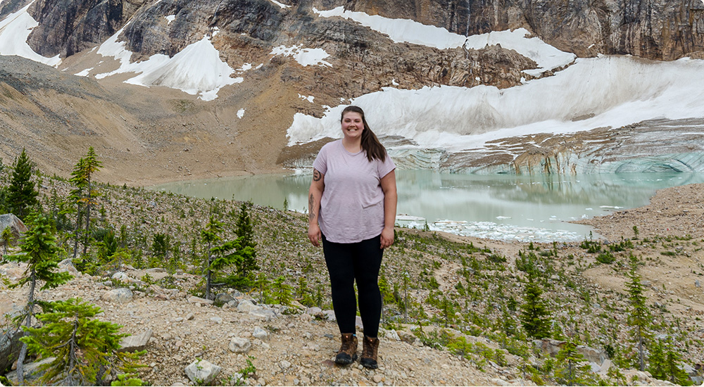 Kaila Walton staying in front of the mountain lake wearing Merrell hiking shoes.