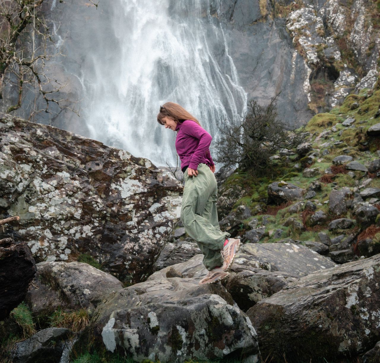Woman climbing rocks near a waterfall