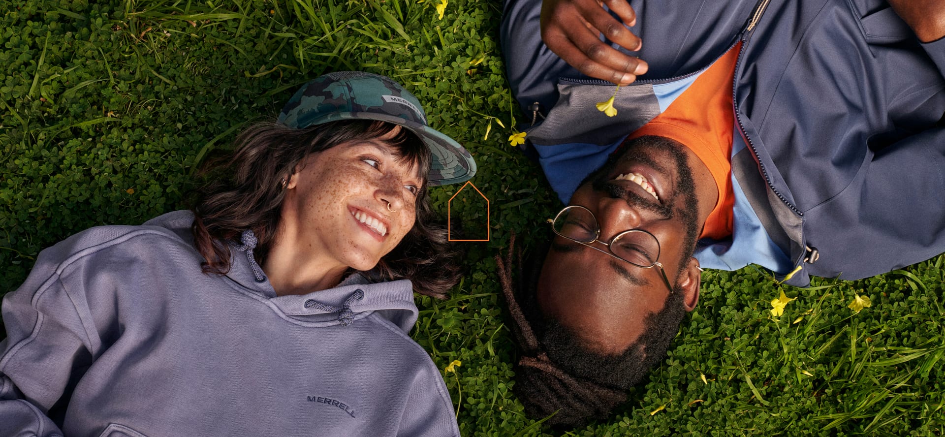 Two people laying together in the grass looking happy. One is holding a clover.