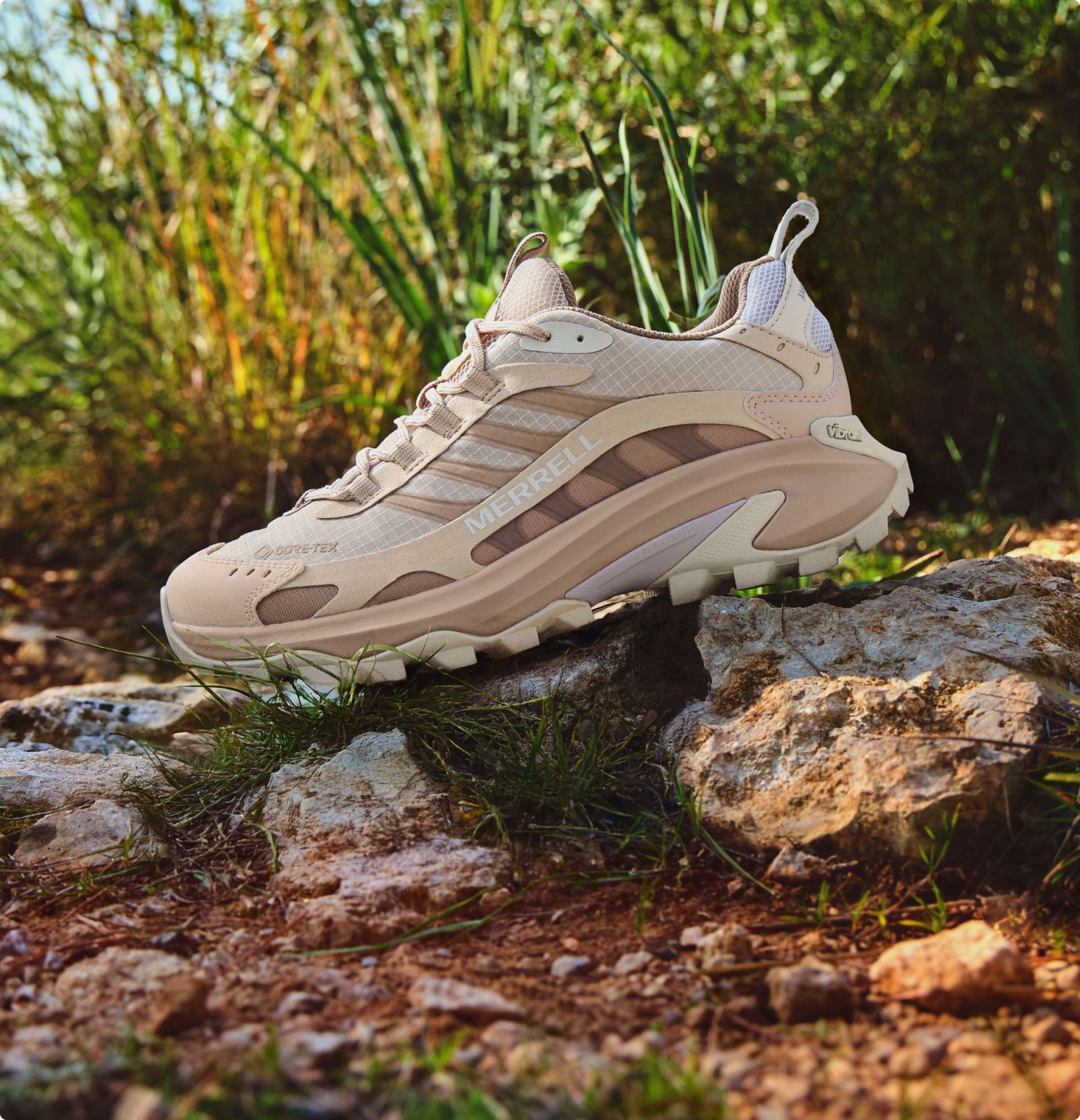 Bota de senderismo Merrell Moab Speed 2 sobre una roca con vegetación de fondo