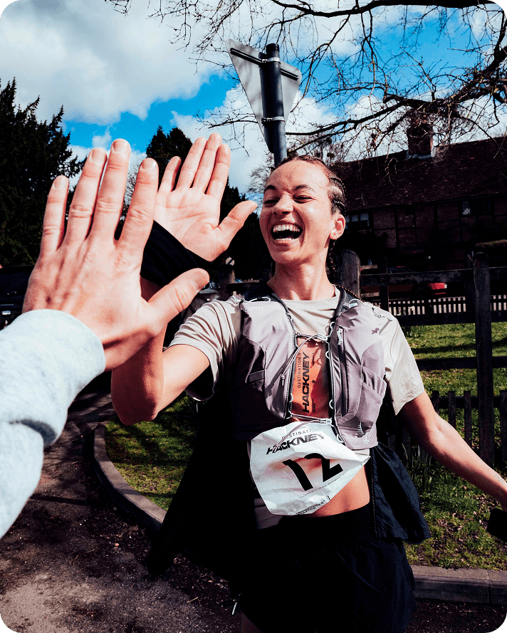 A woman running in a race high fiving another person.