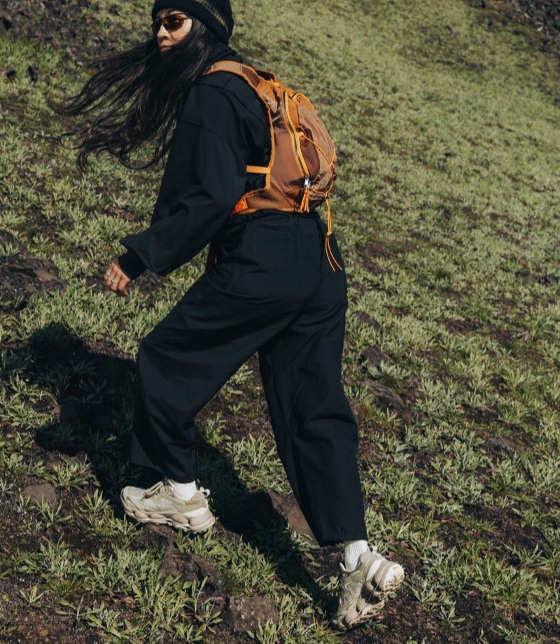 Hiker with an orange backpack walking through a green field