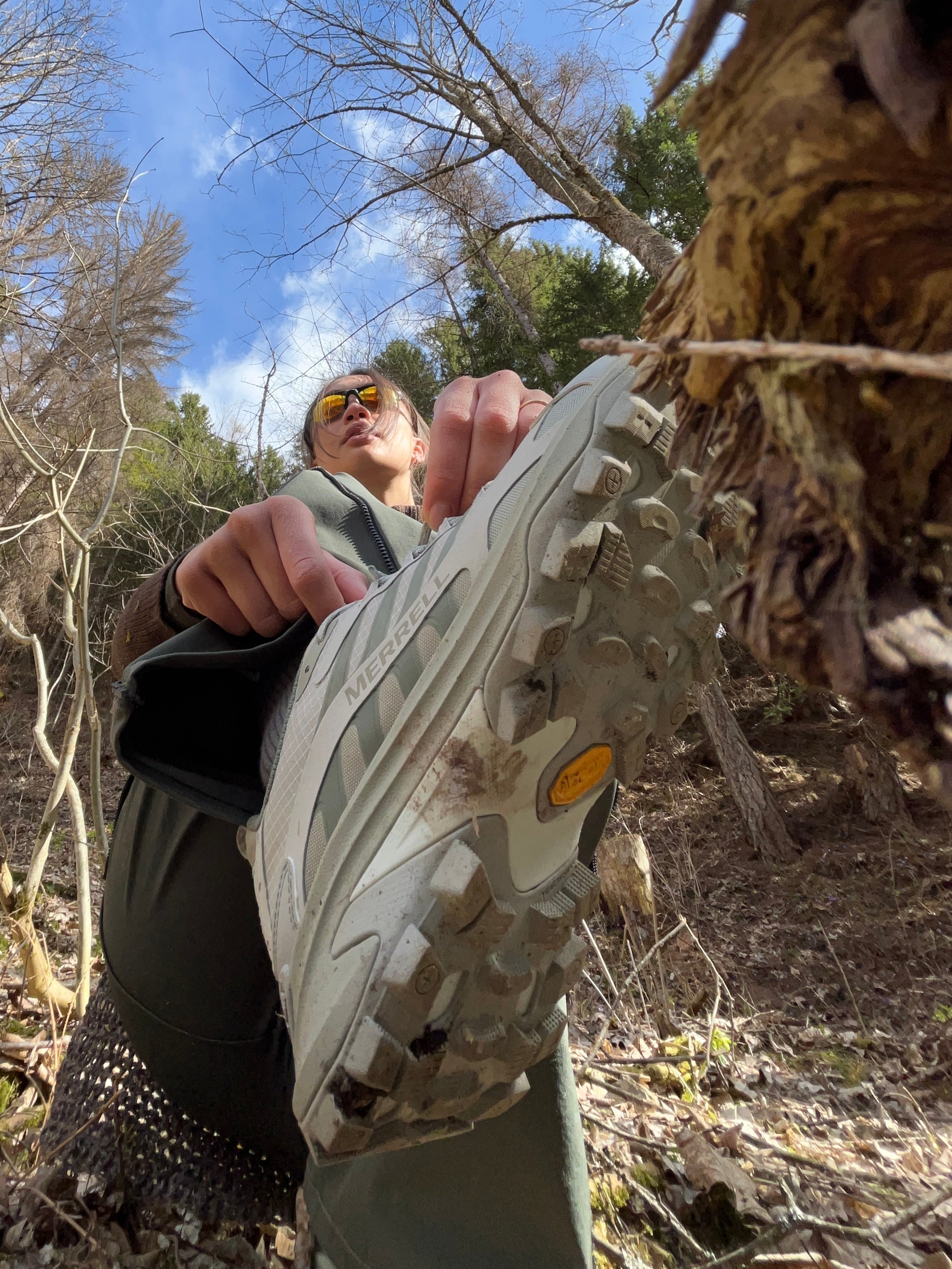 A woman showing the sole of a Merrell hiking shoe while climbing.