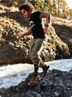 Person sitting on a ledge near water wearing Merrell gear, looking cool.