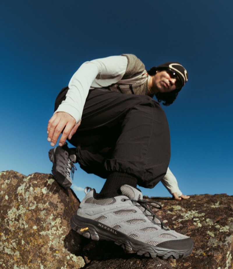 Hiker crouching on rocks wearing Merrell shoes
