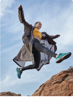 Woman jumping across rocks wearing Merrell hiking boots