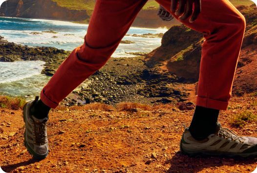 a person's legs in red pants and black socks on a rocky cliff