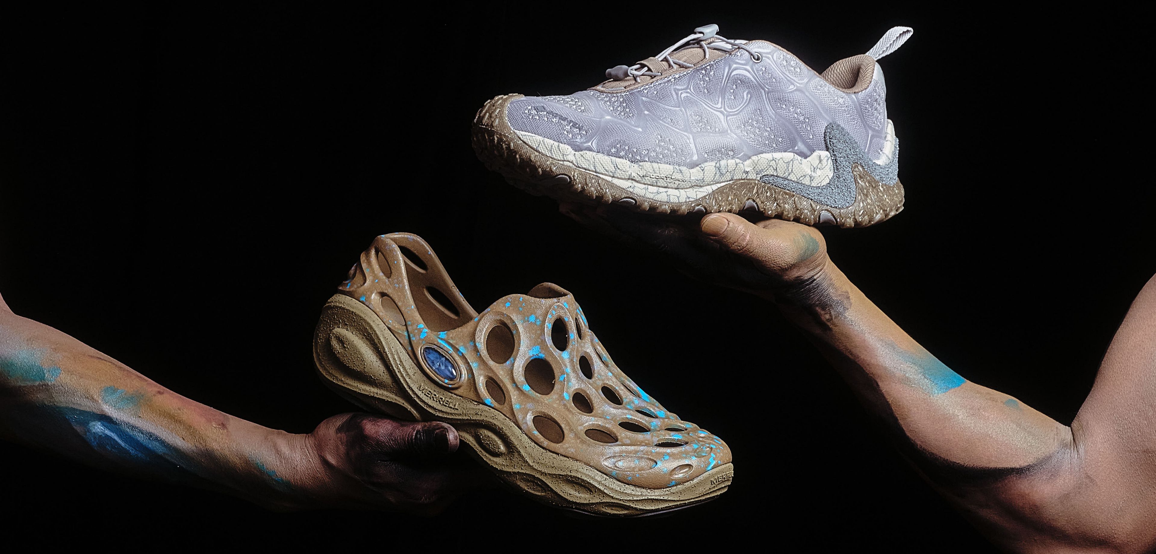 Merrell x P.A.M shoes being held up against a dark background