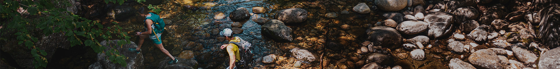 two hikers, one male one female, hide across a river bed jumping from rock to rock, on a sunny summer day