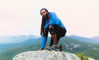 Will Robinson is crouching on top of a boulder on a mountain top.