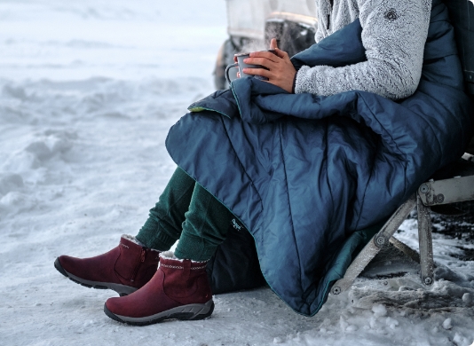 Person sitting in the snow with a blanket.