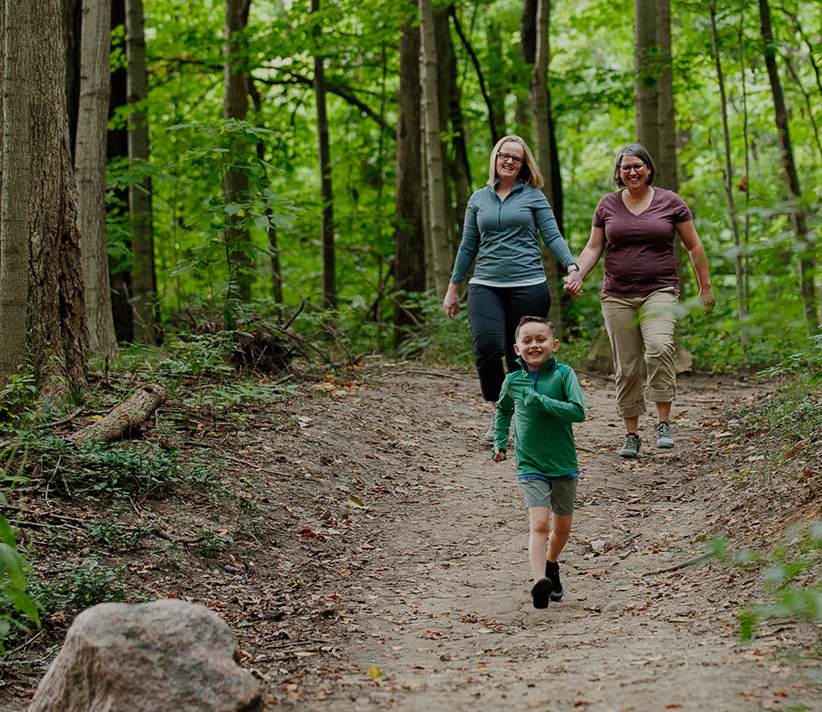 Two women holding hands, hikeing with a kid.
