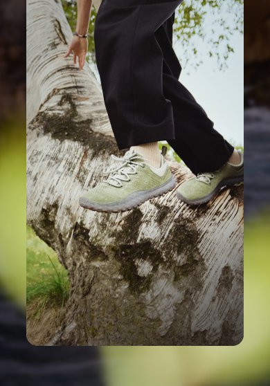 Person in olive green Merrell shoes walking along a fallen birch log.