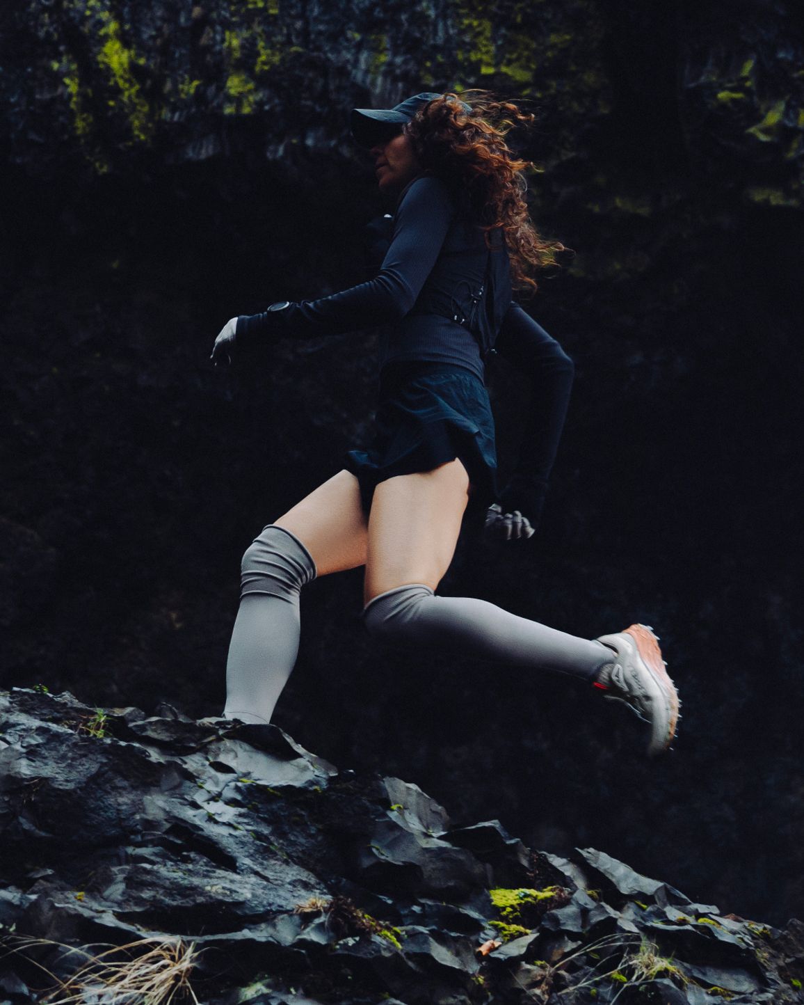A trail runner crossing rocky ground beside a waterfall.