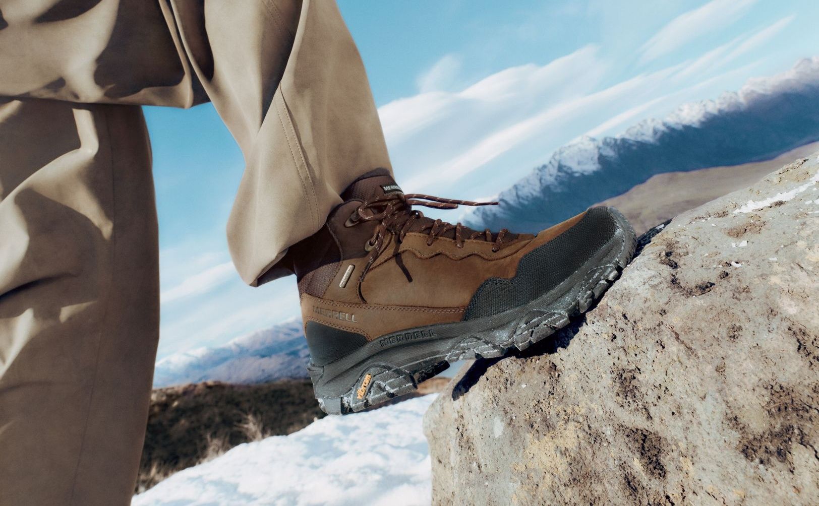 Brown Merrell boots on a rock in a snowy mountain landscape.
